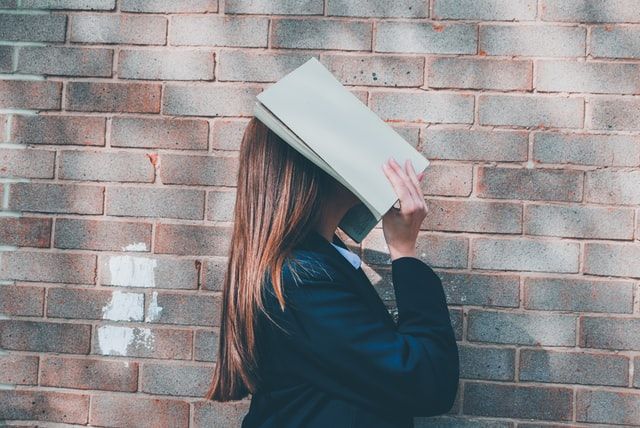 woman holding book covering her face