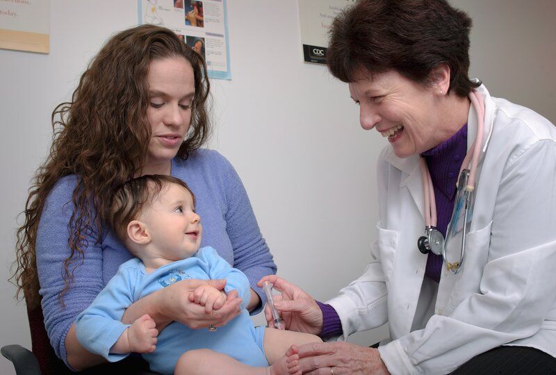 a smiling pediatrician giving a baby a vaccine