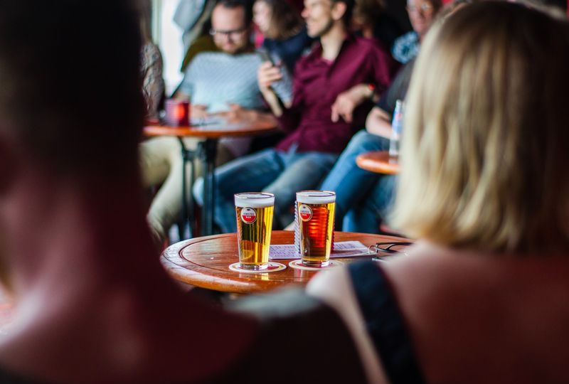people sitting in bar smiling and talking with two beers on center table