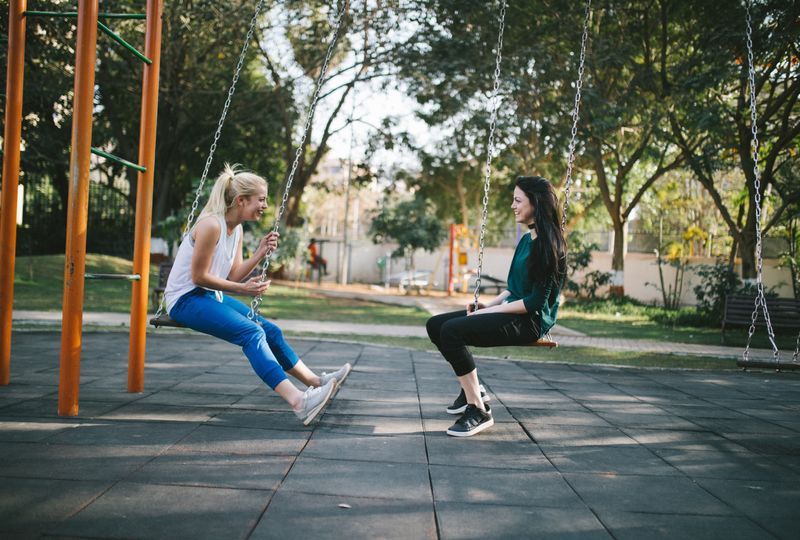 two young women in conversation while sitting on swings in a playground