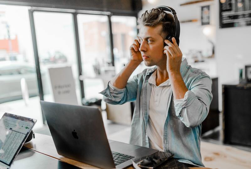 Man putting on headphones with laptop in front of him