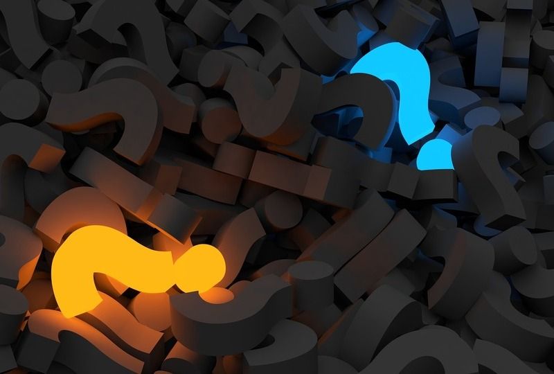 A pile of black question marks with a lit up blue and orange question mark in the pile