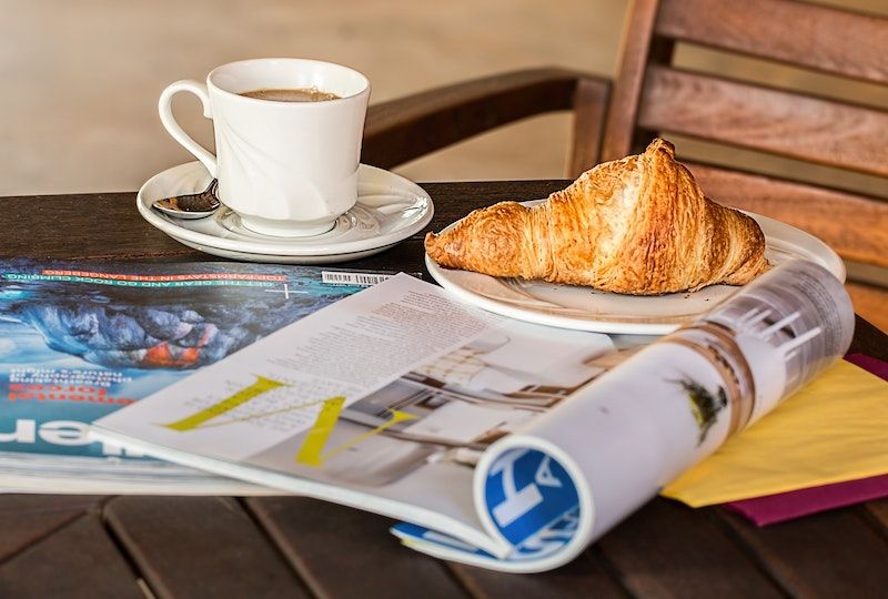 Magazine lying open on a table with a coffee and a croissant next to it