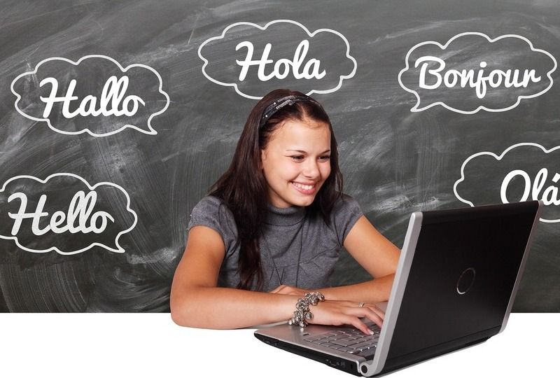 A woman on a computer learning languages with words on a chalkboard behind her
