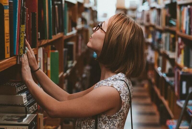 Young woman looking for a book in a library aisle