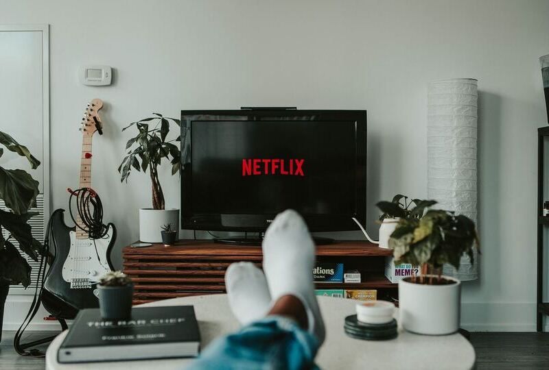 A man's feet on the coffee table with the Netflix logo on the screen in the background
