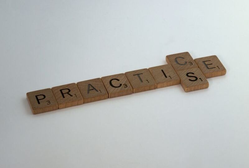 Scrabble tiles that spell out the word 'practice' with an added s tile
