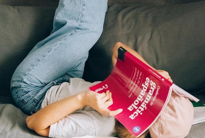 A woman lying on a couch with a Spanish grammar book over her face