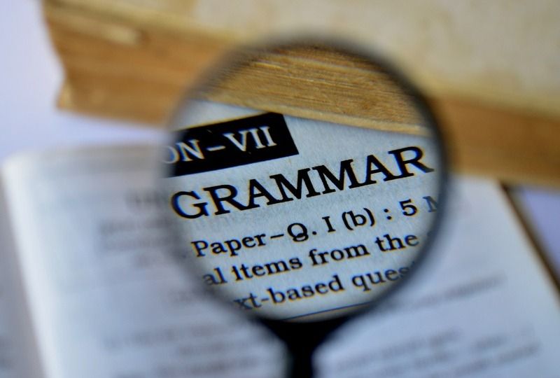 A magnifying glass over a book that is focusing in on the word 'Grammar'