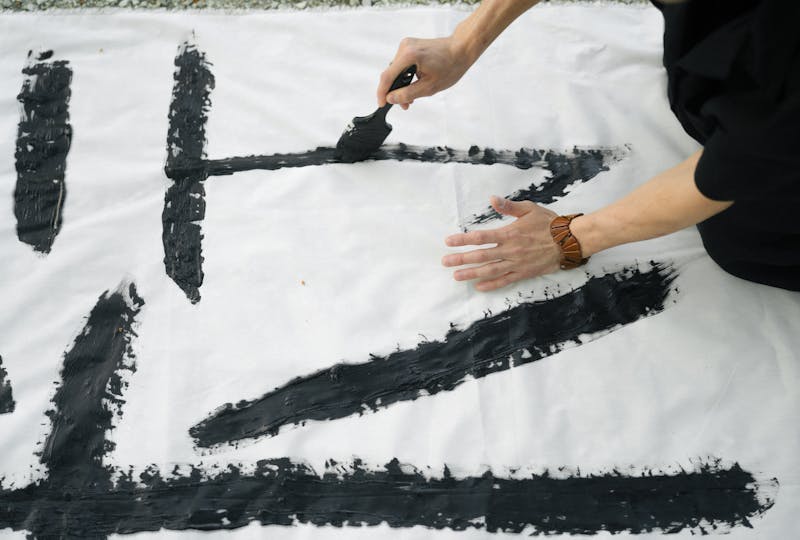 person doing japanese calligraphy on white textile