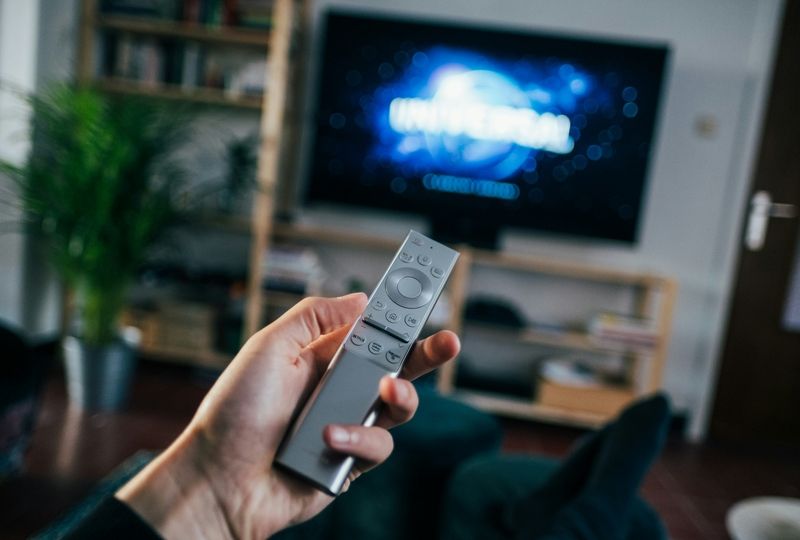 Man holding a remote sitting in front of tv watching a movie