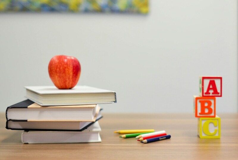 A stack of books with an apple on top on a desk